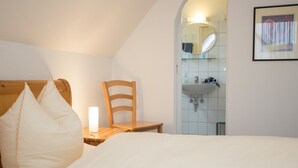A bedroom with a wooden headboard, a wooden chair, a bedside table with a lamp, and a view of a bathroom with a sink and mirror.