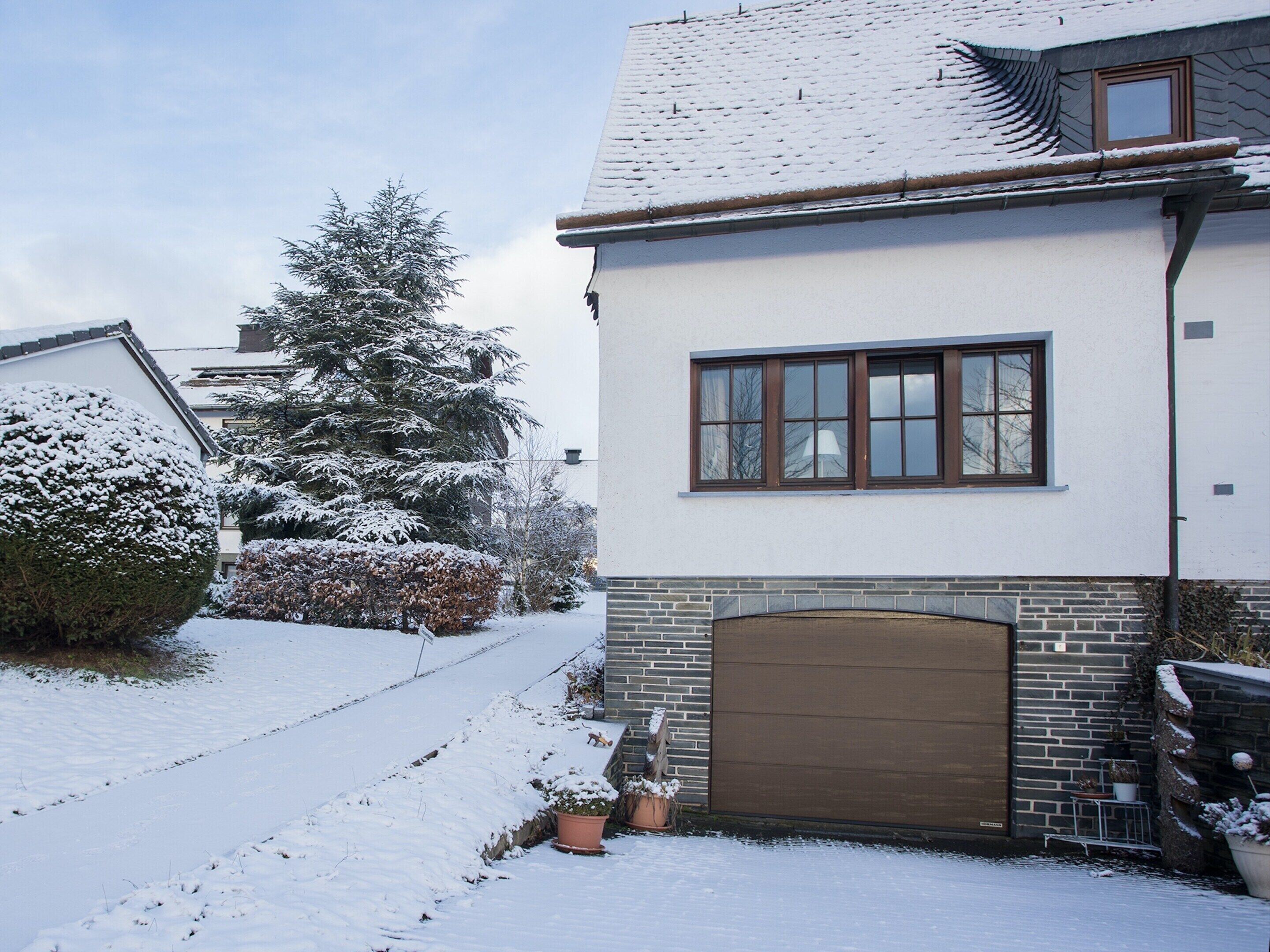 Un immeuble résidentiel dont le toit est recouvert de neige, qui possède une cheminée en briques et une porte de garage.