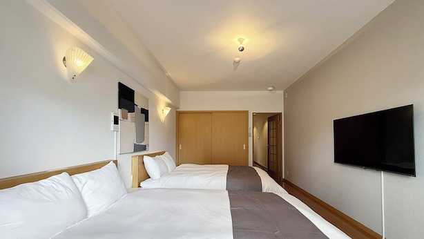 Ein Hotelzimmer mit zwei Betten, einem Fernseher und einem Flur, der in ein weiteres Zimmer führt.
