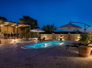Piscina exterior con suelo de piedra, rodeada de sillones de playa y sombrillas.
