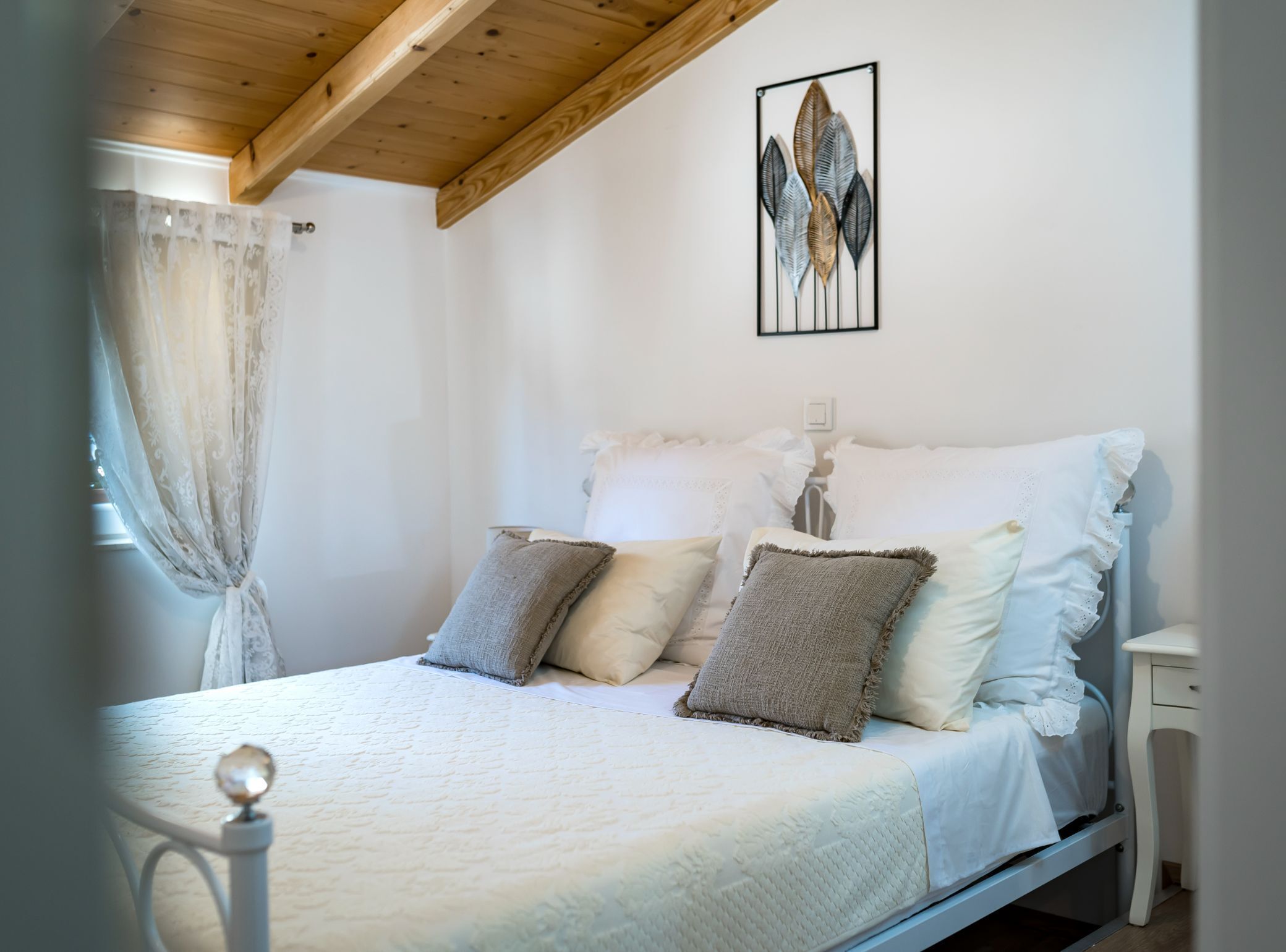 Un dormitorio con cama, almohadas, una mesita de noche y una obra de arte en la pared.