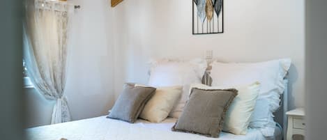 Un dormitorio con cama, almohadas, una mesita de noche y una obra de arte en la pared.