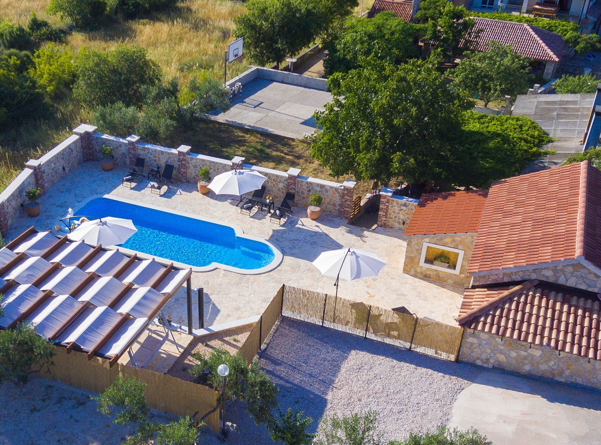 An aerial view of a residential area with a swimming pool, lounge chairs, and a patio area with umbrellas.