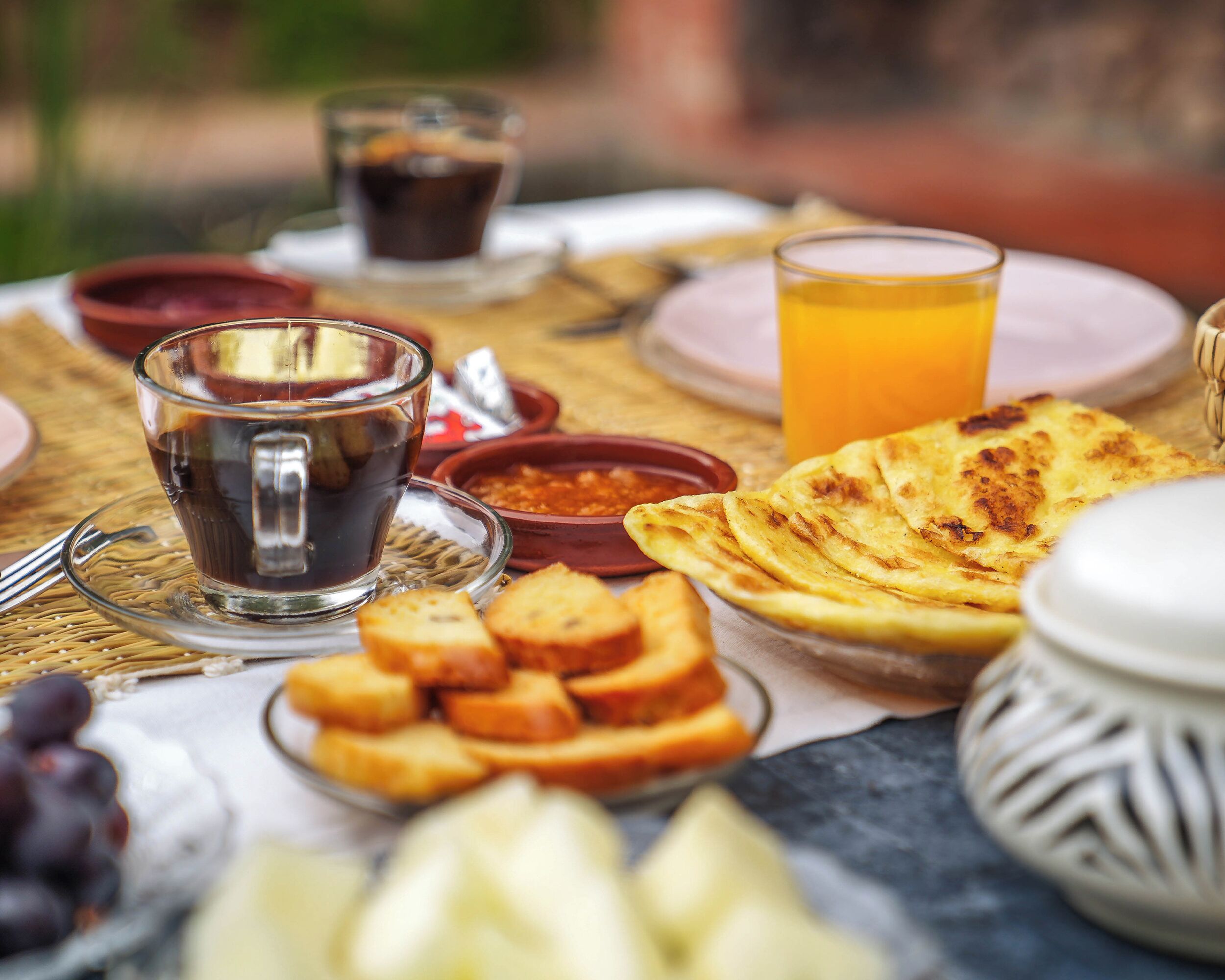 Ein Frühstückstisch mit einer Tasse Kaffee, Orangensaft, Toast und einer Fruchtschale.