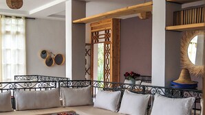 A modern living room with a sofa set, round ottomans, a red carpet, and a decorative mirror. - Sakia Talamanzou (Gmassa)