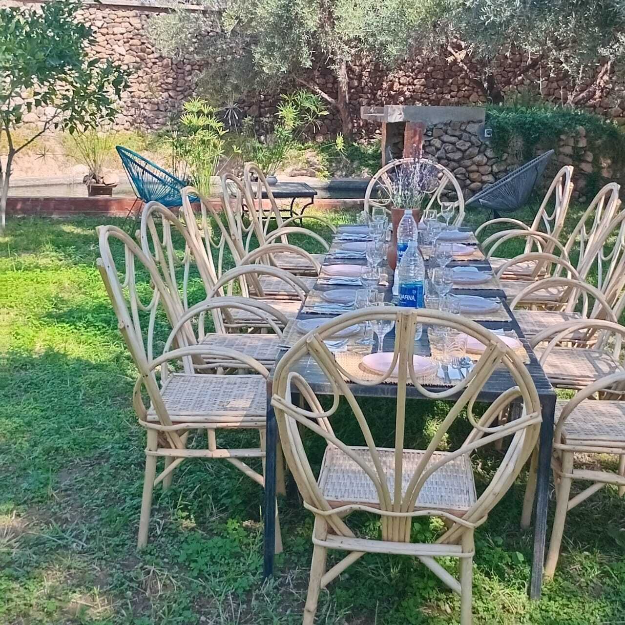 An outdoor dining area with wicker chairs and a long table set for a meal.