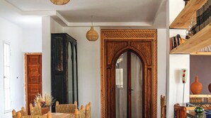 A dining area with a patterned floor, a wooden dining table with woven chairs, and a decorative wooden door. - Sakia Talamanzou (Gmassa)