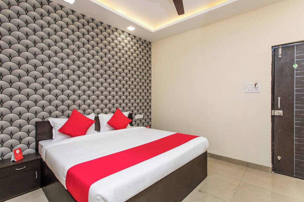 Ein Hotelzimmer mit geprägtem Wandpapier, einem Bett mit weißer und roter Bettwäsche, einem Nachttisch und einer Tür.