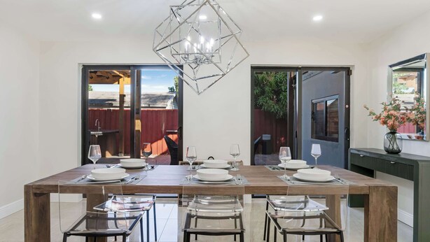 Uma sala de jantar com mesa de madeira, cadeiras transparentes e um lustre geométrico.