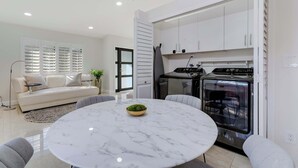 Uma cozinha moderna com armários brancos, forno embutido e área de jantar com mesa de mármore.