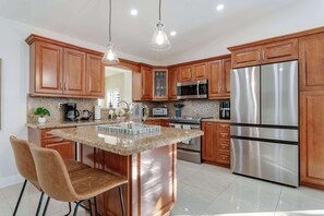 A modern kitchen with wooden cabinets, stainless steel appliances, a granite countertop, and pendant lighting.