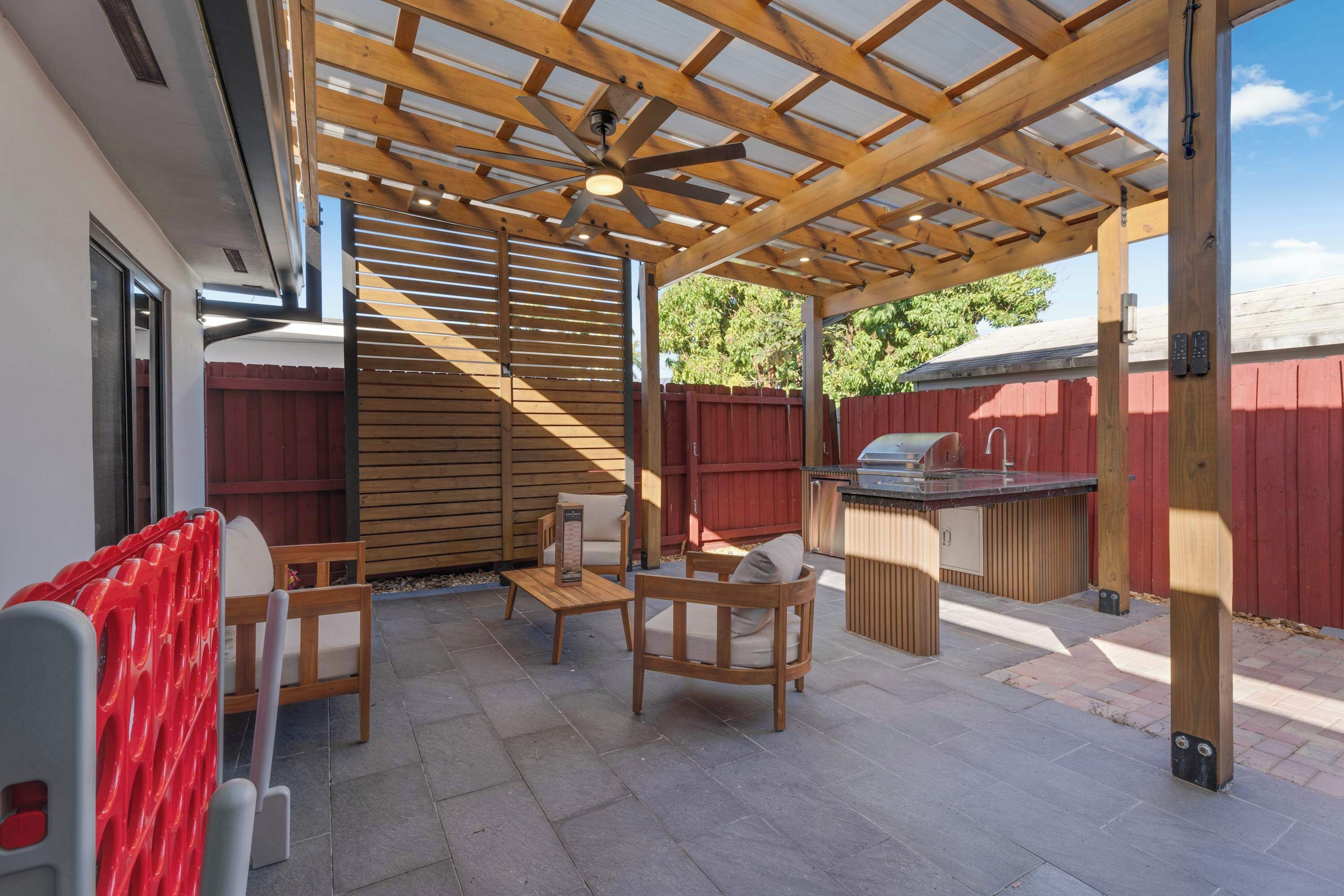 En overdækket terrasse med en ventilator, træmøbler og en grill.