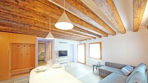 Een moderne woonkamer met een houten plafond, een grijze bank, een eettafel met een witte tafelkleed en een televisie op een dressoir.