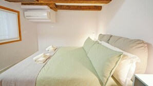 Een slaapkamer met een bed, kussens, een raam en een airconditioning.