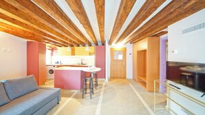 Een modern interieur met zichtbare houten balken, een keukenhoek, een zithoek met een bank en een tv-meubel.