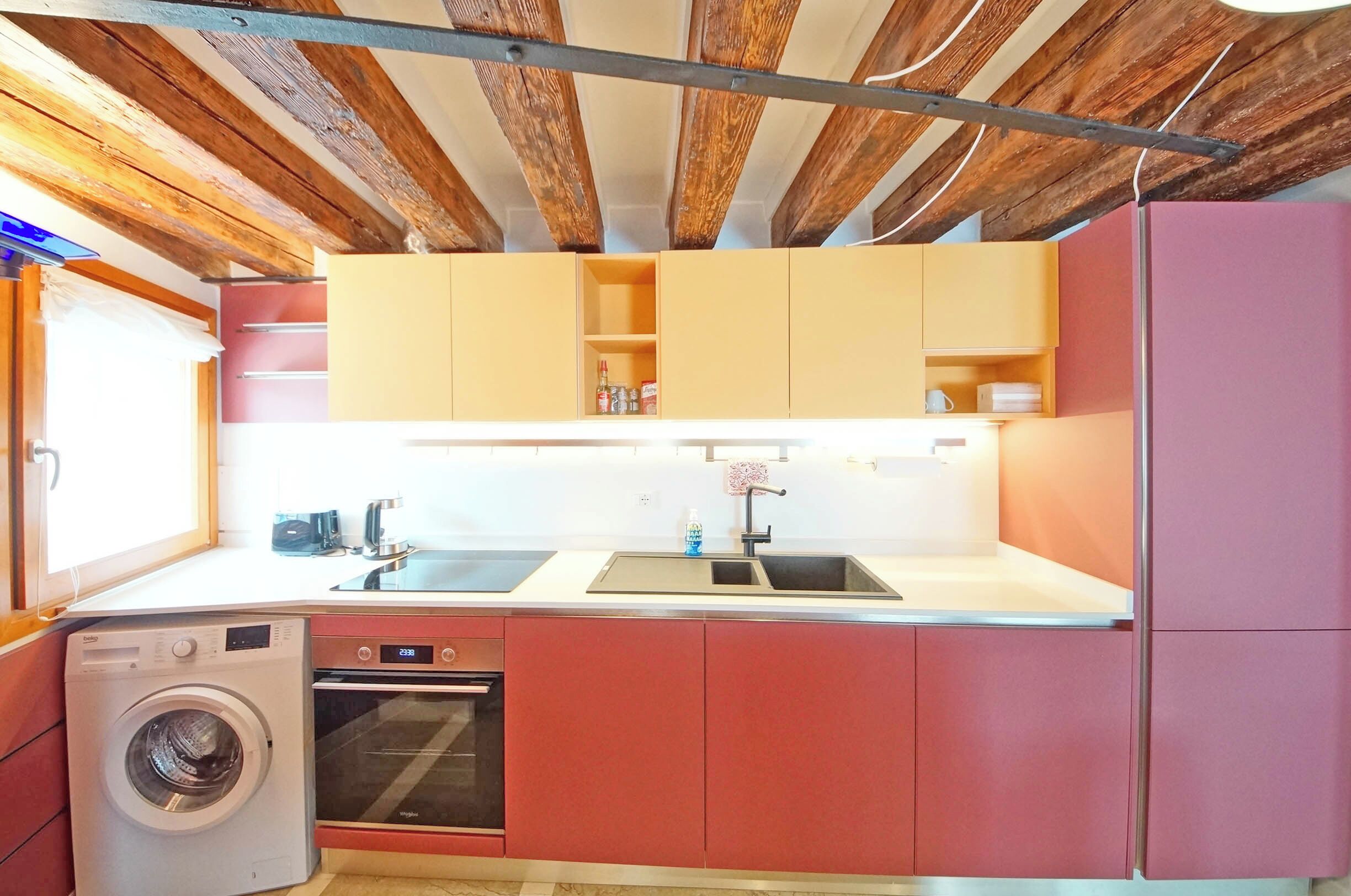 Cocina compacta con lavadora, horno y lavabo con grifo moderno.
