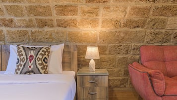 Un dormitorio con una cama, una mesita de noche con lámpara, una silla roja y una pared de piedra.