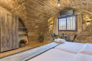 A cozy room with a stone ceiling, a bed, a wooden wardrobe, a small table with chairs, and a window with curtains. - Timberwood Studio in Batroun (Batroun)