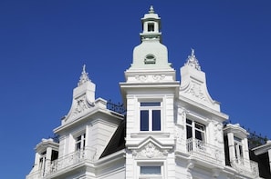 Un edificio blanco con detalles arquitectónicos ornamentales, incluyendo una torre central con aguja y dos alas simétricas.