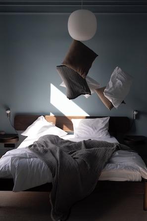 Un dormitorio con cama, almohadas, una colcha y una lámpara colgante.