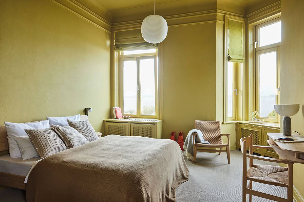 Een slaapkamer met een bed, twee stoelen, een bureau en een raam met uitzicht.