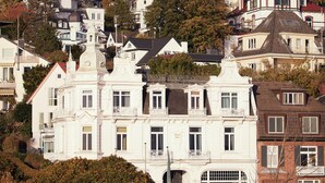 Un bâtiment blanc doté d’un balcon et d’un toit rouge, entouré d’autres bâtiments et d’arbres.