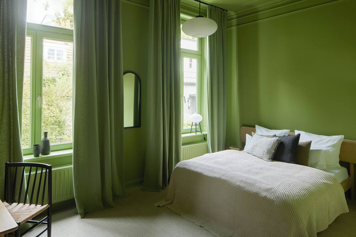 Een kamer met een bed, een stoel, een raam met gordijnen en een radiator.