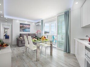 A modern living room with a dining area, a kitchen, and a balcony with a view.