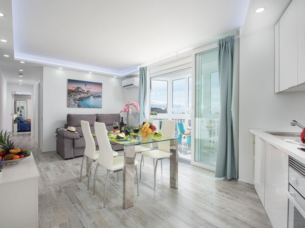 A modern living room with a dining area, a kitchen, and a balcony with a view.