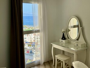 A room with a large window, a white vanity with a mirror, a small stool, and a lamp. - Exquisite renovated 2-bedroom apt with pool, air conditioning and WiFi in Las Américas (Playa de las Américas)