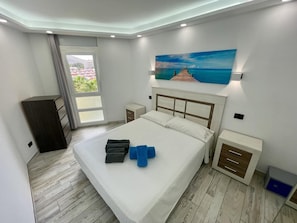 Ein Schlafzimmer mit Bett, Nachttisch, Kommode und einem Gemälde eines Piers.