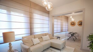 Un salon moderne avec un canapé d’angle beige, une petite table d’appoint et un coin repas comprenant une table et des chaises en verre.