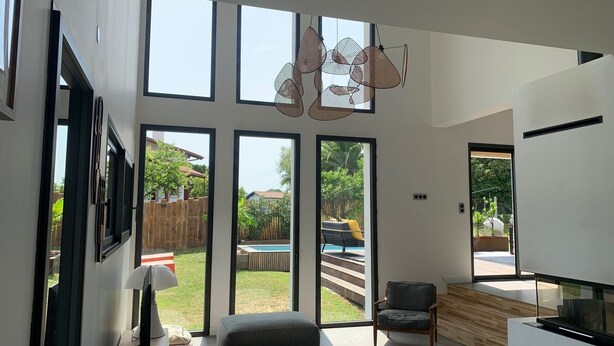 A spacious living area with large windows, a modern kitchen, and a view of a backyard with a pool.