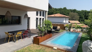 A modern house with a swimming pool, outdoor seating, and a garden.