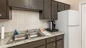 Een keuken met donkere kastjes, een witte koelkast, een koffiezetapparaat en een granieten aanrecht.