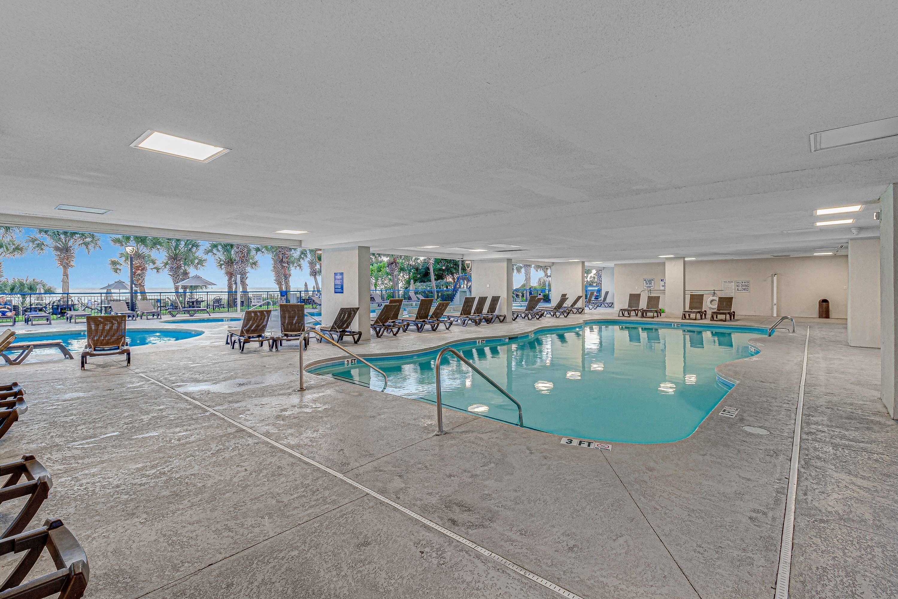 An indoor swimming pool with lounge chairs and a view of palm trees.