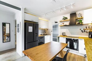 A modern kitchen with a wooden dining table, white cabinets, and a black refrigerator.