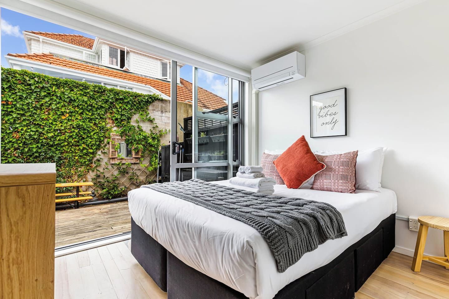 A modern bedroom with a large bed, a view of a garden, and a sliding glass door leading outside.