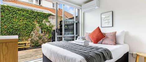 Un dormitorio moderno con una cama grande, vistas a un jardín y un ventanal corredero que da al exterior.