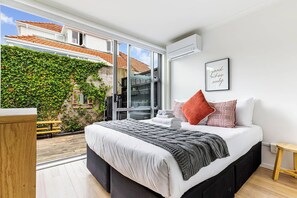 A modern bedroom with a large bed, a view of a garden, and a sliding glass door leading outside.