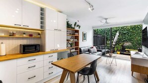 Una cocina moderna con armarios blancos, encimera de madera y una zona de comedor con mesa y sillas de madera.