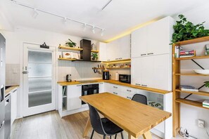 Moderni keittiö, jossa on valkoiset kaapit, puinen ruokapöytä ja seinään integroitu kirjahylly.