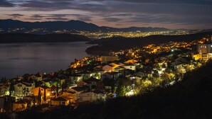 A coastal town at night with illuminated buildings and a view of the sea and mountains in the background. - Villa V (Crikvenica)
