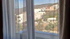 A window with sheer curtains, offering a view of buildings and a hilly landscape. - Villa V (Crikvenica)