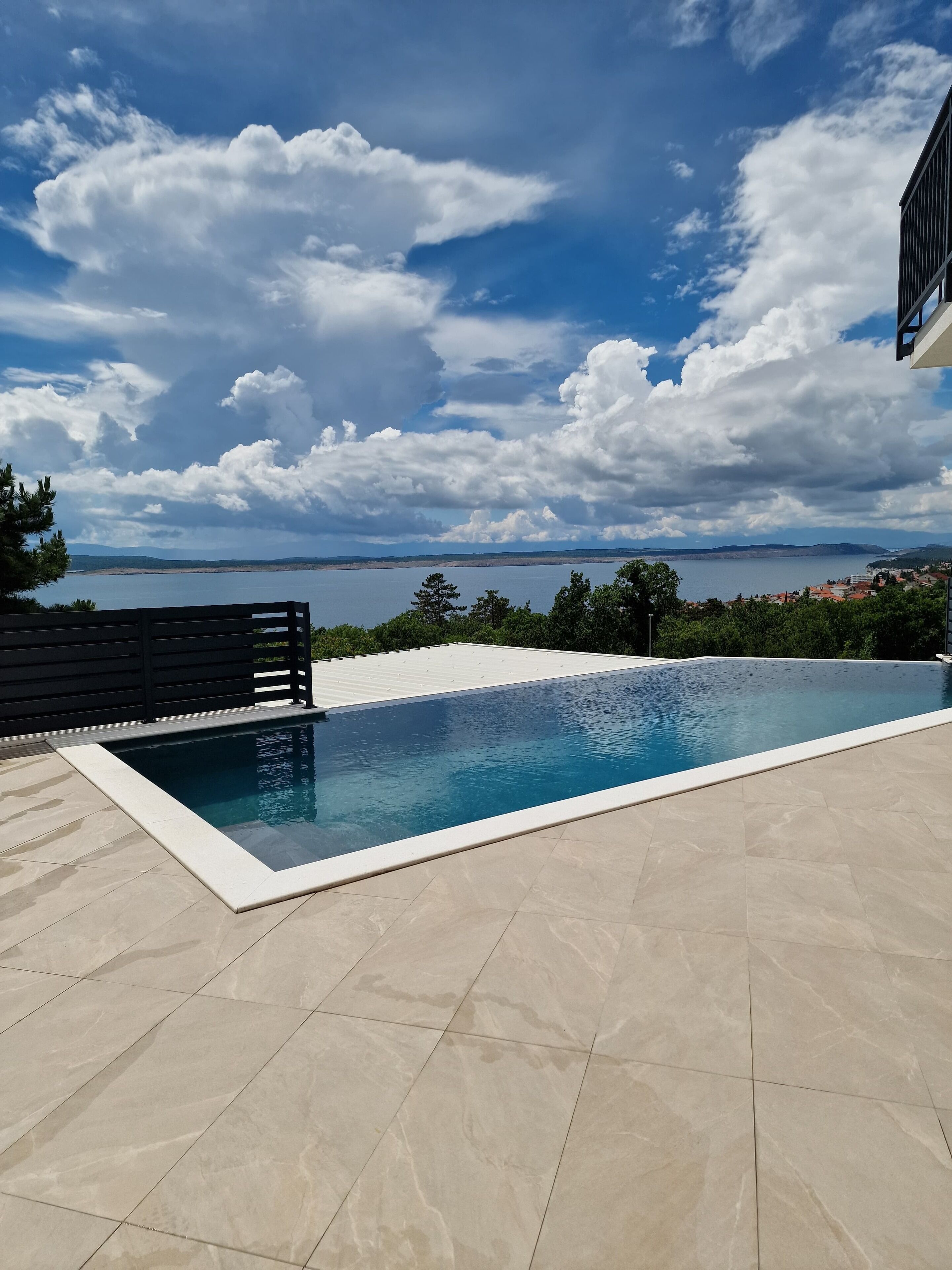 A swimming pool with a view of the sea and distant hills.