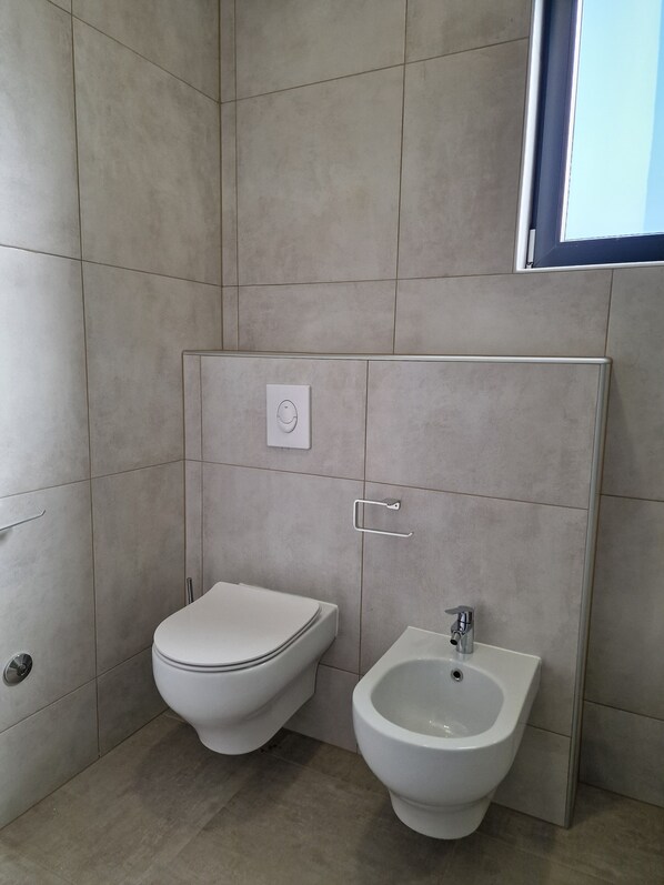 Un baño moderno con inodoro, bidé, paredes con azulejos y una ventana con vistas.