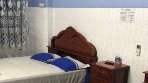 Ett hotellrum med två separata sängar, en sänggavel i trä, ett litet träbord vid sängen och en telefon som är monterad på väggen.