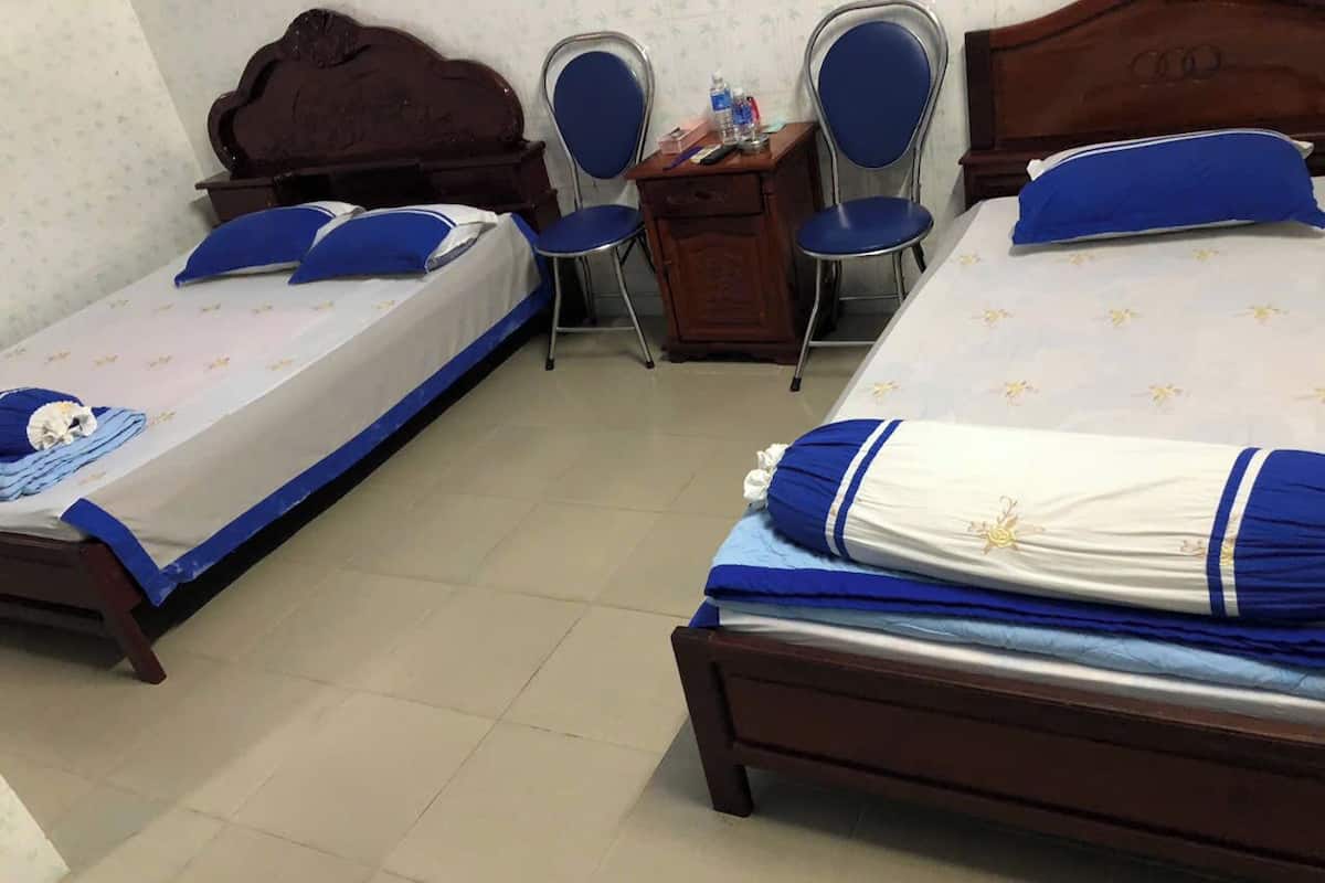 Ein Zimmer mit zwei Betten, jeweils mit blauer und weißer Bettwäsche, einem hölzernen Kopfteil und einem kleinen Schreibtisch mit Stuhl.