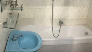 Ett badrum med ett vitt badkar, ett blått handfat och en duschslang.