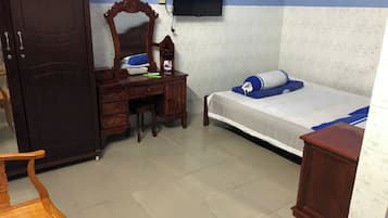A bedroom with a bed, a wooden desk, a chair, a wardrobe, and a television mounted on the wall.